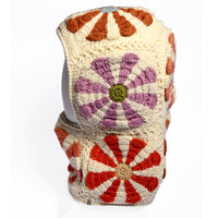 The Hand Crochet Petal Hood is a cream-colored crocheted balaclava adorned with large orange, red, and purple flower patterns and charming crochet daisies throughout, shown on a white mannequin head against a plain white background.