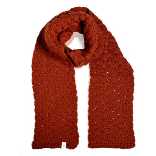 The Hand Crochet Veil Scarf, crafted from rust-colored Merino wool with a textured bobble stitch and lacy pattern, is laid out flat on a white background. The scarf is looped at the top and features a small white tag at one end.