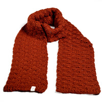 A Hand Crochet Veil Scarf crafted from soft Merino wool in a rich rust shade is displayed against a white background. The scarf showcases a repeating bobble stitch pattern for subtle texture and is finished with a small white tag sewn onto one end.