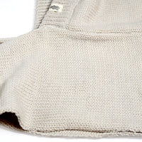 A close-up of the beige Hand Loom Nomad Hood Scarf showcases its intricate knitted texture and stitching patterns, with a small white and black tag sewn near the top edge. The detailed craftsmanship highlights what makes this lambswool scoodie both cozy and stylish.