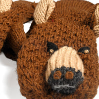 A close-up of the Hand Crochet Grizzly Mittens, featuring a brown knit design crafted to resemble a grizzly bear’s face, with black eyes, a beige snout and ears, and black nostrils. Made from hand-crocheted wool, these charming kids mittens are displayed against a white background, with the edge of another mitten partially visible.