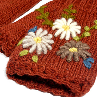 Close-up of the Hand Knit Bloom Mittens in a rust-colored yarn, showcasing intricately embroidered white and brown flowers with green leaves. The image highlights the rich texture of the knit and the detailed embroidery, emphasizing the skilled craftsmanship behind these charming handmade mittens.