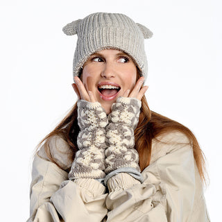A woman in a beige coat wears a gray knit hat and Multi Color Flower Crochet Fingerless Gloves, holding her hands to her face and looking off to the side with an excited expression.
