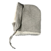 The Hand Knit Glide Hood is a light gray seed-stitch lambswool hood with a soft white fleece lining, featuring a front flap and two knit ties, shown laid flat on a white background.