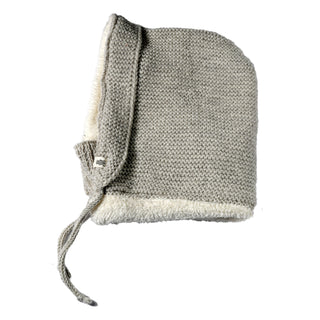 The Hand Knit Glide Hood is a light gray seed-stitch lambswool hood with a soft white fleece lining, featuring a front flap and two knit ties, shown laid flat on a white background.