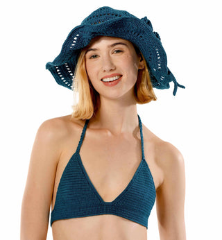 A smiling woman is wearing a blue hand-crocheted sun hat and a matching Bikini Top - Solid, making for a perfect addition to any summer wardrobe. She is looking directly at the camera against a plain white background.