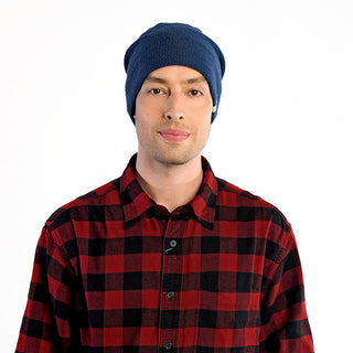 A man wearing The Depp Slouch, a blue slouchy beanie, and a red and black plaid shirt stands facing the camera against a plain white background.