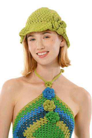 A person stands smiling, wearing a crocheted green and blue halter top with a diamond pattern and flower accents. They also wear the One Side Turned Up Hat in matching green, featuring flower details. They have light brown shoulder-length hair and light denim jeans.