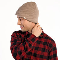 A person wearing the Hand Knit Bond Hat in beige and a red and black plaid shirt stands against a white background, looking down with one hand touching the back of their neck.