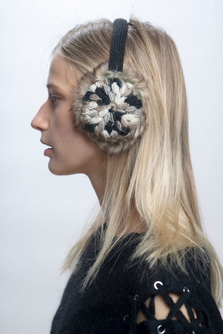 A person with long blonde hair in profile wears Hand Crochet Kaleidoscope Earmuffs—black and white with faux fur lining—paired with a black lace-up sleeve top against a plain light background.