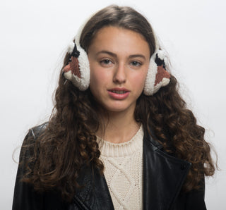 A person with long curly hair wears a black leather jacket, a cream hand-knit wool sweater, and white Hand Knit Fox Earmuffs with a bird design, standing against a plain white background.