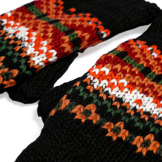 Close-up of the Hand Knit Explore Mittens—two black wool mittens featuring an orange, red, green, and white patterned design across the front in a classic Fair Isle style—displayed on a white background.