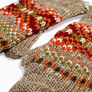 Close-up of two Hand Knit Explore Mittens featuring a beige base and colorful Fair Isle patterns in red, orange, green, and white yarn. The mittens are displayed on a white surface.