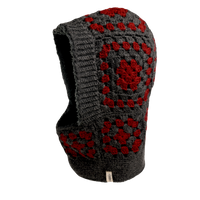 The Hand Crochet Patch Hood, crafted from wool in gray with red square patterns, is displayed against a white background. It features an opening for the face and a small white tag near the bottom edge.