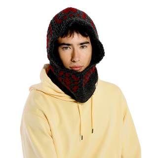 A person wearing a yellow hoodie and the Crochet Patch Hood, which features a dark knit design with red and gray patterns, covering their head and neck. The background is solid black.