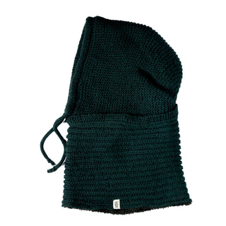 The Hand Knit Halo Reverse Hood in dark green features a textured knitted pattern, drawstring ties on one side, and a small rectangular white label near the bottom edge, displayed on a white background.