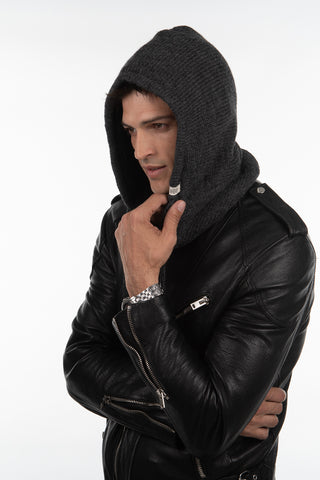 Man wearing a black leather jacket with the Hand Loom Hero Hood stands against a plain white background, looking to the side and touching his chin.