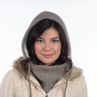 Woman with dark hair wears the beige Hand Loom Hero Hood, featuring a fur-trimmed hood and matching knit scarf, facing forward against a plain white background.