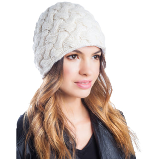 A woman with long brown hair wearing a white wool cable knit Holden Beanie, looking to the side, against a white background.