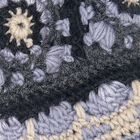 Close-up of textured crochet fabric for Dreams Hand Crochet Handwarmers, featuring dark, light gray, cream, and purple yarn in a starburst or flower-like stitch pattern.