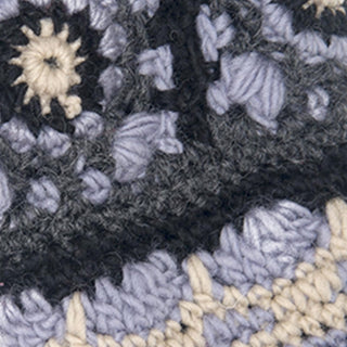 Close-up of textured crochet fabric for Dreams Hand Crochet Handwarmers, featuring dark, light gray, cream, and purple yarn in a starburst or flower-like stitch pattern.