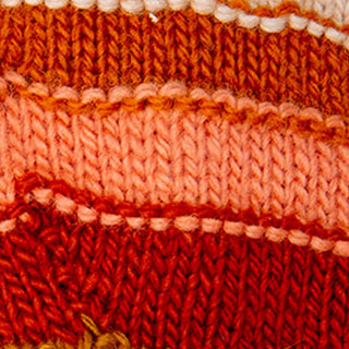 Close-up of knitted fabric in red, orange, and peach stripes from Short Cuff Fingerless Gloves handmade in Nepal. Texture and individual stitches of the knit pattern are clearly visible.