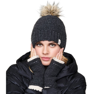 Woman wearing a winter hat with a pom-pom and a puffy jacket while holding her cheeks with Les handwarmers.