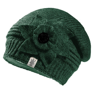 The Monroe Hat is a green knitted wool beanie featuring a large floral accent with a black button, ribbed brim, and a white logo tag. This stylish accessory is handmade in Nepal.