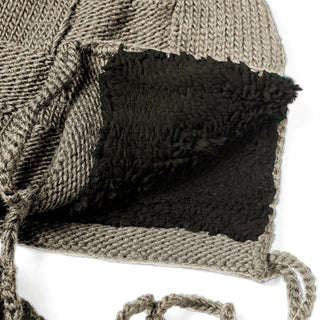 A close-up of the Hand Knit Nest Hat reveals its interior, lined with soft black fleece-like fabric. Two braided strings are attached to this cozy, sherpa-lined earflap hat.
