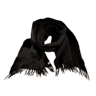 A Merino Fringe Scarf, expertly handcrafted in Nepal, is displayed on a white backdrop. The scarf, in classic black, boasts fringed edges and is made from soft merino wool, woven for ultimate comfort and style.