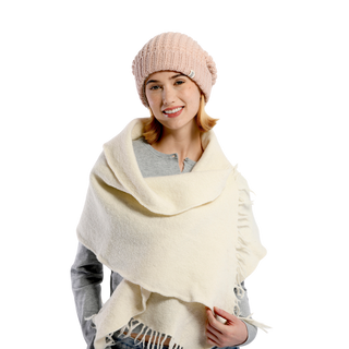 A person wearing a light pink knitted hat, a gray long-sleeve shirt, and a cream-colored Merino Fringe Scarf is smiling. The background is plain and not visible. The scarf, handmade in Nepal from 100% merino wool, complements the outfit perfectly.