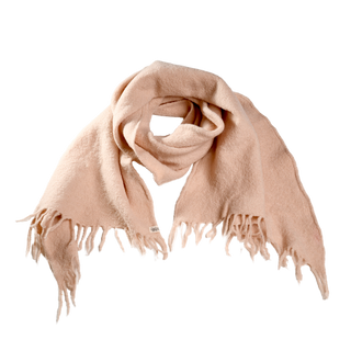 A light pink Merino Fringe Scarf, showcasing frayed edges, is displayed. Handmade in Nepal from 100% merino wool, the scarf is loosely folded to highlight its soft texture and features a small tag near one end.