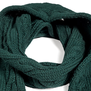 The Hand Knit Plush Scarf is loosely coiled against a white background, highlighting its deep green hue, thick textured yarn, and detailed cable knit pattern. Made from soft Merino wool, this scarf offers both warmth and style for chilly days.