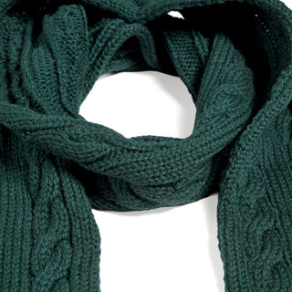 A Hand Knit Plush Scarf in dark green, featuring intricate cable stitching and fringe ends, is displayed in a loose loop against a white background, highlighting the soft merino wool texture and detailed craftsmanship.