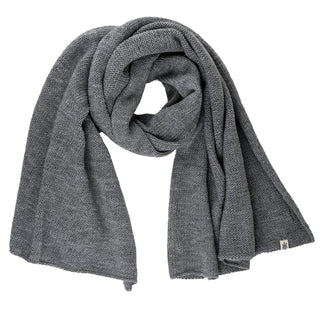 A Hand Loom Air Wrap Scarf in gray is laid flat and loosely folded, displaying a small white fabric tag on one end.