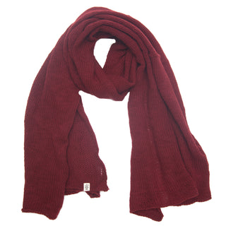 The Hand Loom Air Wrap Scarf, in deep red, is hand-knit and laid flat on a white background. It features a small tag near one end and looks soft, thick, and ideal for staying warm in cold weather.