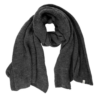 The Hand Loom Air Wrap Scarf in dark gray merino wool is laid flat with a loose, circular fold at the center, its ends draped to the sides and a small white fabric tag near one end.
