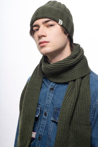 A person in a green knit hat and Hand Loom Laurent Scarf, handmade in Nepal, over a blue denim button-up shirt looks at the camera with a neutral expression against a plain white background.