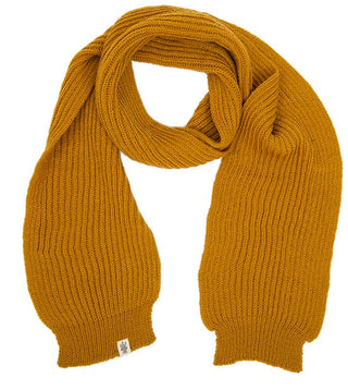 The Laurent Scarf is a mustard yellow, ribbed knit merino wool scarf laid flat on a white background. It features wide ribbing, a small tag at one end, and highlights expert Nepalese craftsmanship.