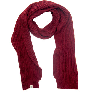 The Hand Loom Laurent Scarf is a long, thick, ribbed knit in deep red, handmade in Nepal with a small white tag—soft, cozy, and perfect for staying warm in cold weather.