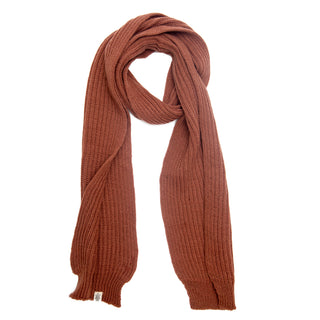 A long, thick Hand Loom Laurent Scarf in ribbed knit and solid rust brown is laid flat with one end looped over the other. A small white tag accents this handmade Nepalese merino wool scarf.