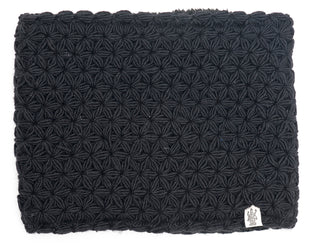 A black textured I See Stars Neckwarmer with a repetitive geometric pattern and handmade in Nepal, featuring a visible brand label in the lower right corner.