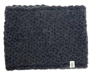 A dark gray textured I See Stars Neckwarmer with a star-shaped pattern design and a small white label in the bottom right corner displaying a logo, handmade in Nepal.