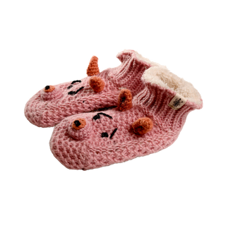 A pair of pink, hand-knit Piggy Slippers made of wool, featuring a charming dinosaur design with small orange spikes and black embroidered faces. These cozy slippers come with a fluffy white lining and have a convenient tag on the side, making them the perfect winter accessory.