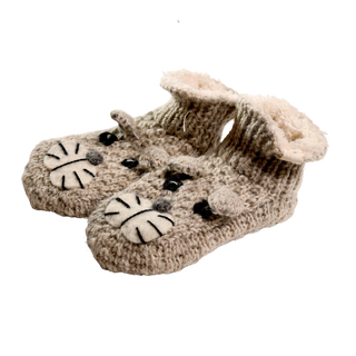 A pair of Shmil The Cat Slippers in beige, hand-knit in Nepal with a plush lining. These adorable baby booties feature a cute tiger face design with black and white details on the top.