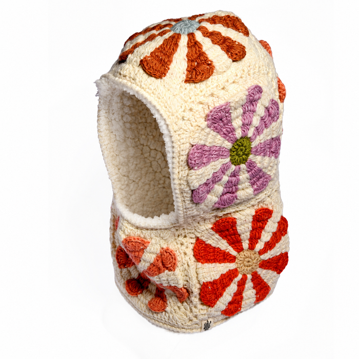 The Hand Crochet Petal Hood is a cream-colored knit balaclava featuring an open face and adorned with large, textured red, orange, and purple flower designs inspired by crochet daisies. It also has a soft sherpa fleece lining for added warmth and comfort.