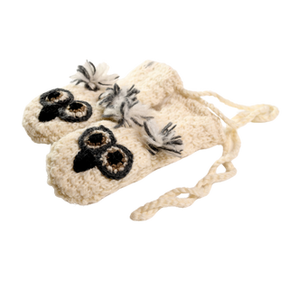 A pair of Crochet Owl Mittens featuring owl faces with black-and-brown eyes on the tops, made from 100% wool in a cream-colored knit design. Hand-made in Nepal, these mittens have a textured pattern and include braided ties for securing them.