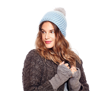 A woman wearing a Dimensions Crochet Beanie w/ Faux Fur Pom, wool, and a cozy, brown sweater gazes to the side.