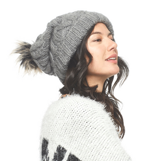A woman wearing a grey Sugar Sugar Slouch sweater and a pom pom hat with a faux fur pom.