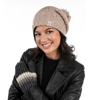 A woman smiling at the camera, wearing a Union Slouch with pom and gloves, handmade in Nepal from merino wool, paired with a black leather jacket.